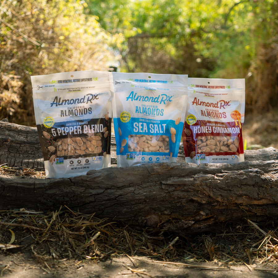 Three packages of almonds sitting on log on a hiking trail.